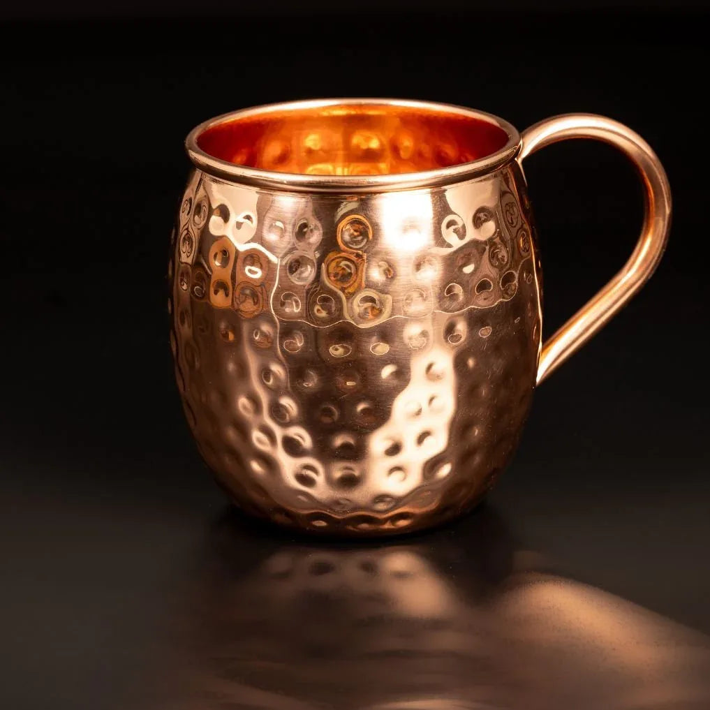 Detail d un mug en cuivre pur martele main montrant les reflets de lumiere sur le relief artisanal et la anse ergonomique