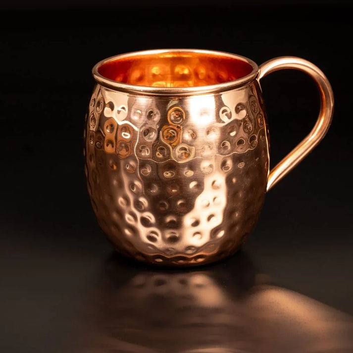 Detail d un mug en cuivre pur martele main montrant les reflets de lumiere sur le relief artisanal et la anse ergonomique