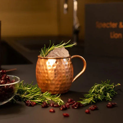 Mug en cuivre massif Lion avec branche de romarin et baies sechees dans une ambiance tamisee mettant en valeur ses reflets flamboyants