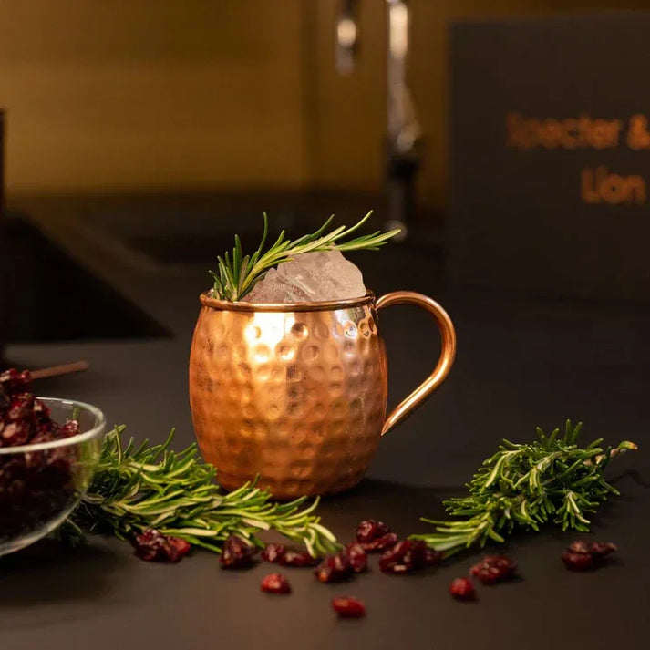 Mug en cuivre massif Lion avec branche de romarin et baies sechees dans une ambiance tamisee mettant en valeur ses reflets flamboyants